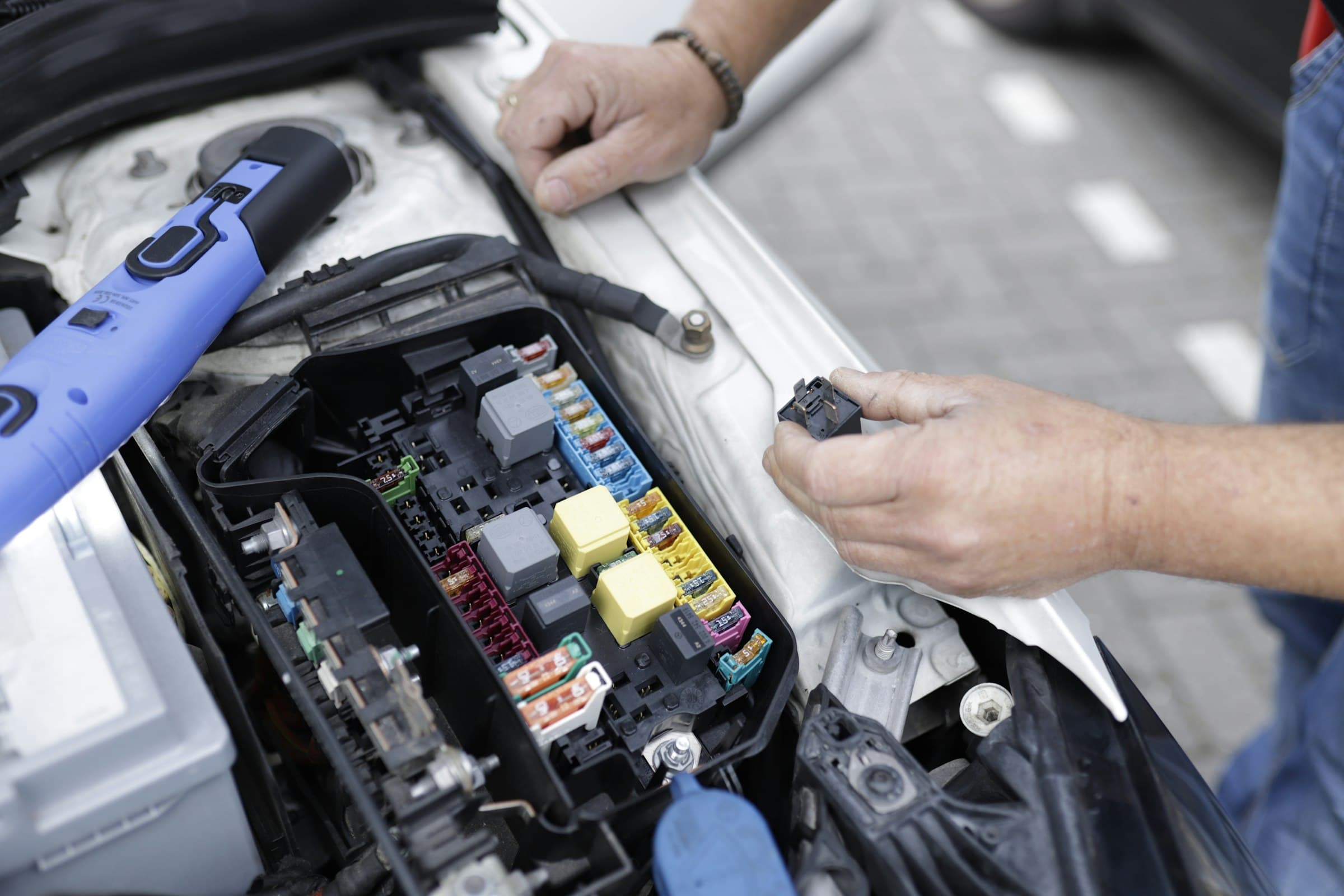 Les mains d'un mécanicien travaillent sur la boîte à fusibles sous le capot d'une voiture.