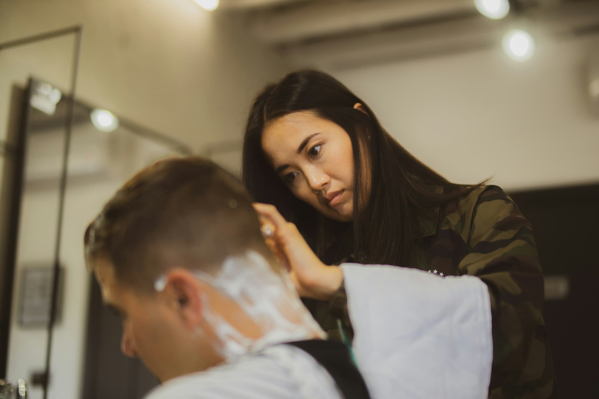 Un coiffeur, dans un salon de barbier moderne, applique de la mousse à raser sur la nuque d'un client.