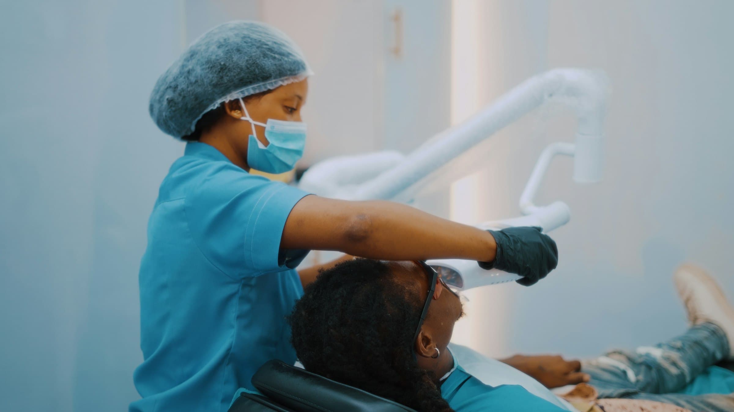 Une hygiéniste dentaire place la lampe au-dessus d'un patient installé dans le fauteuil d'une clinique dentaire.
