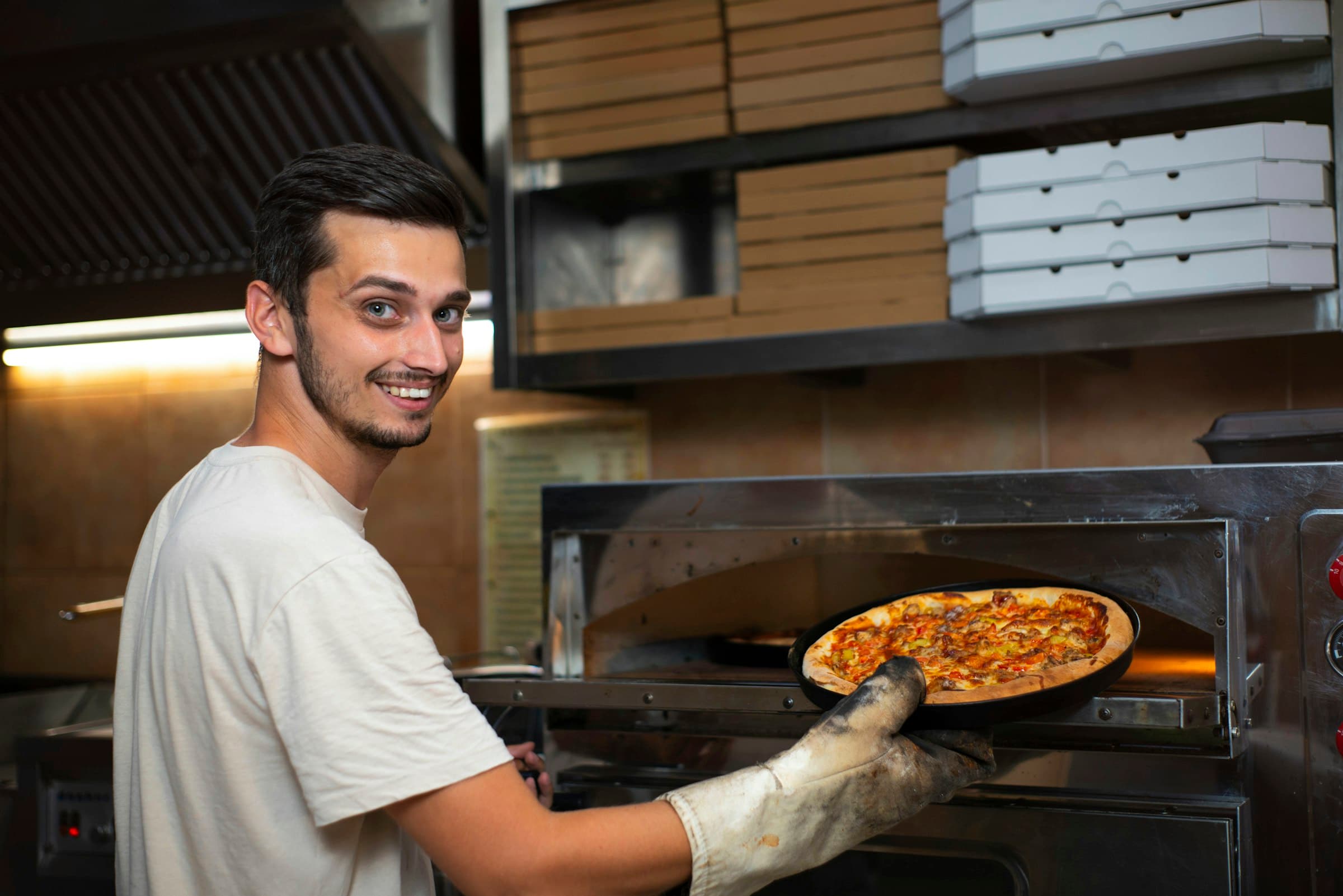 Un pizzaïolo souriant sort une pizza fraîche du four.