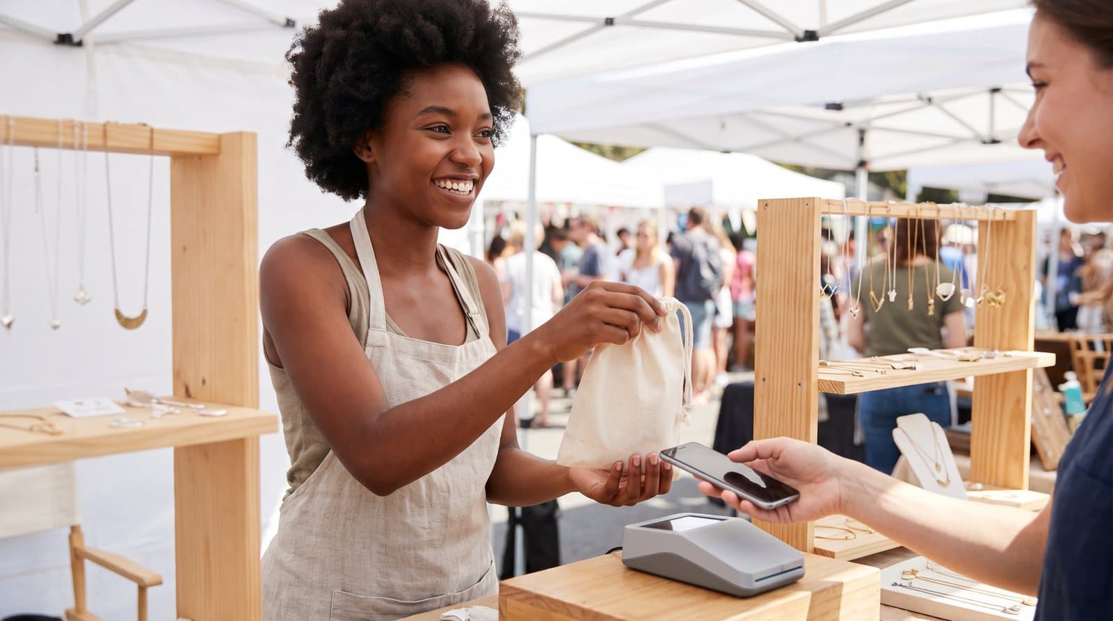 A jewelry maker hands over a purchase at a weekend market stall