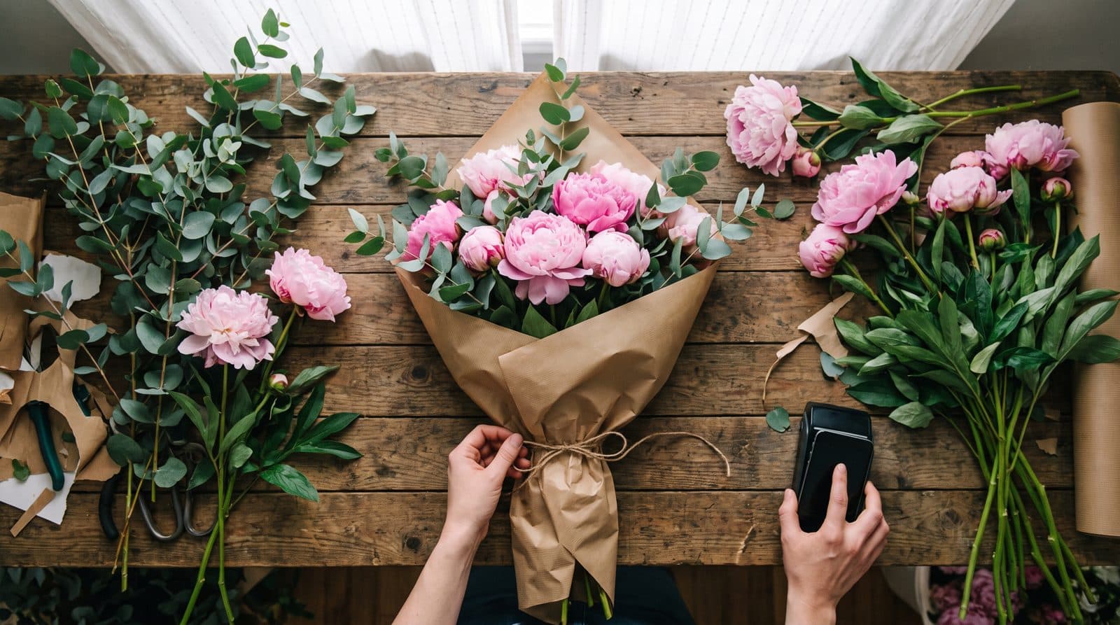 A florist wraps a bouquet while a customer taps a phone on a card terminal
